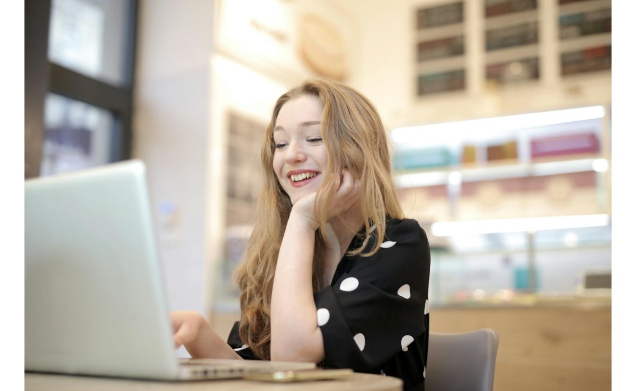 A cheerful woman enjoying her work on a laptop in a brightly lit office environment.