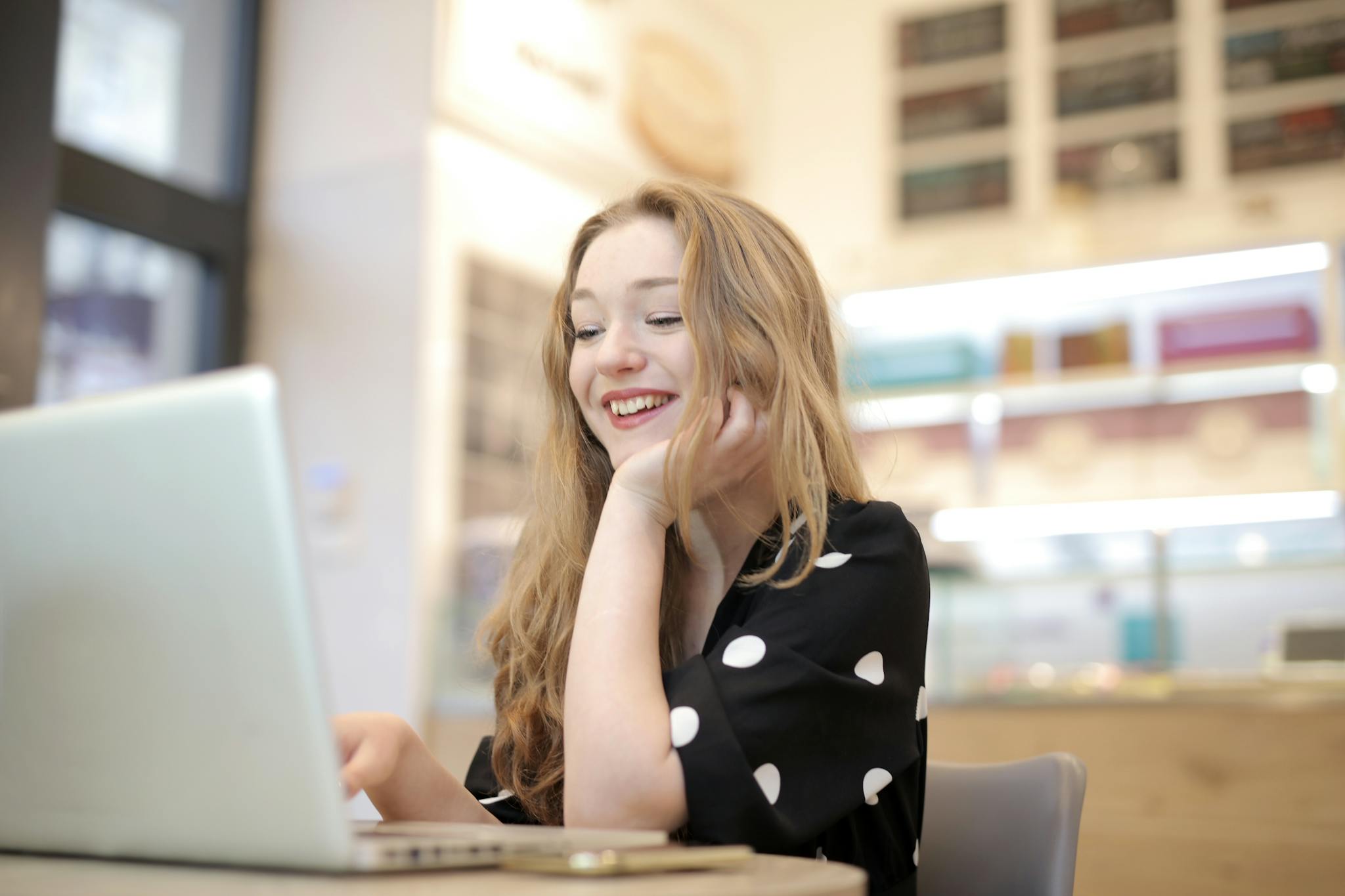 A cheerful woman enjoying her work on a laptop in a brightly lit office environment.